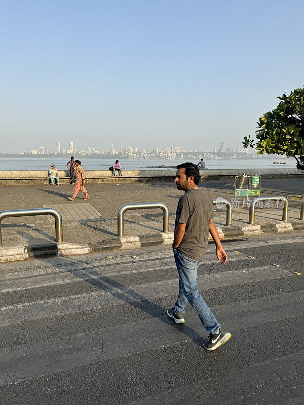 一名印度男子在Marine Drive多车道公路上的斑马线人行横道上行走，c形人行道和混凝土，海堤防御，孟买，印度，海水，建筑物和摩天大楼，孟买，马哈拉施特拉邦